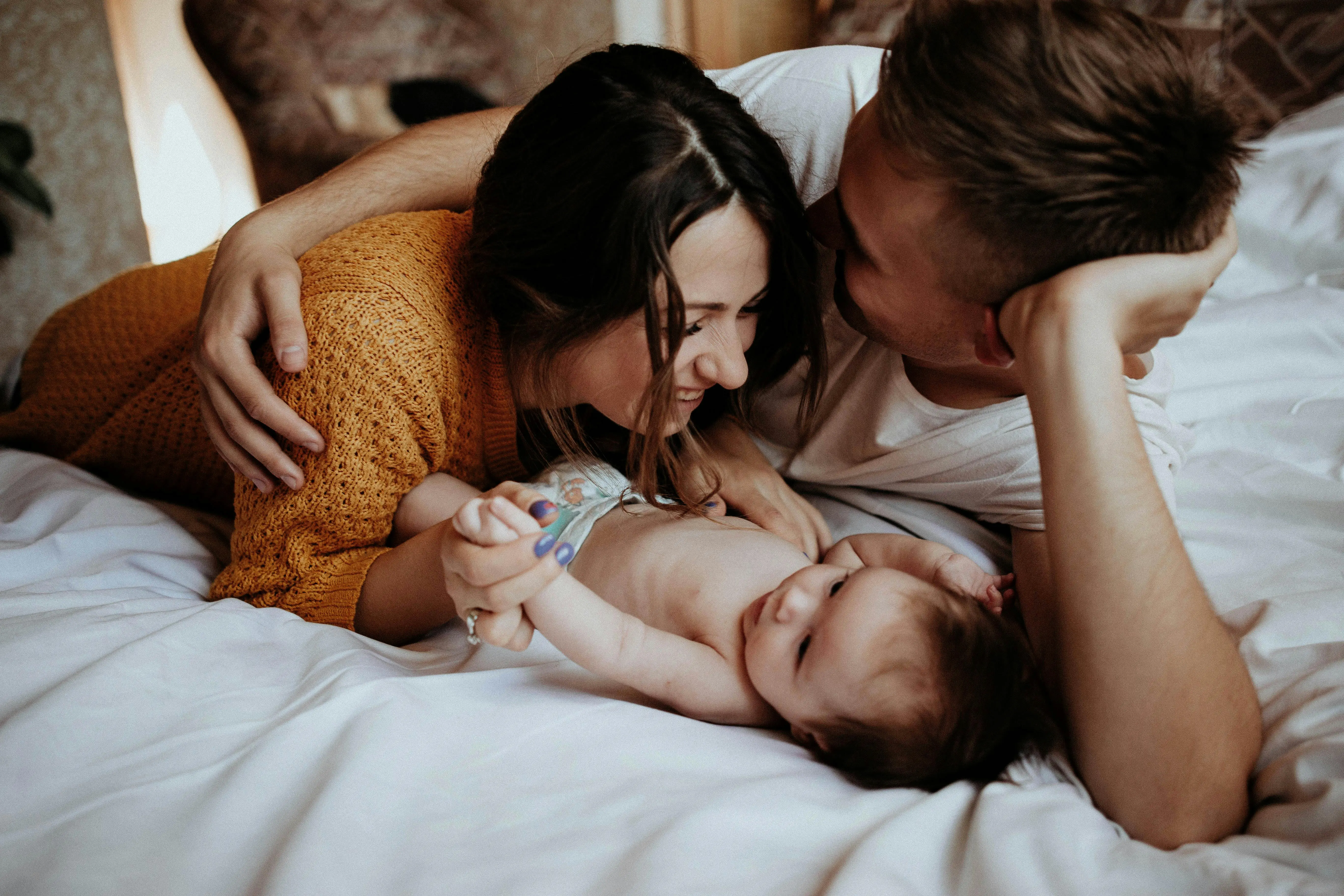 Happy parents lying on a bed with their baby, symbolizing major life transitions like new parenthood as a time when professional cleaning support is especially helpful.