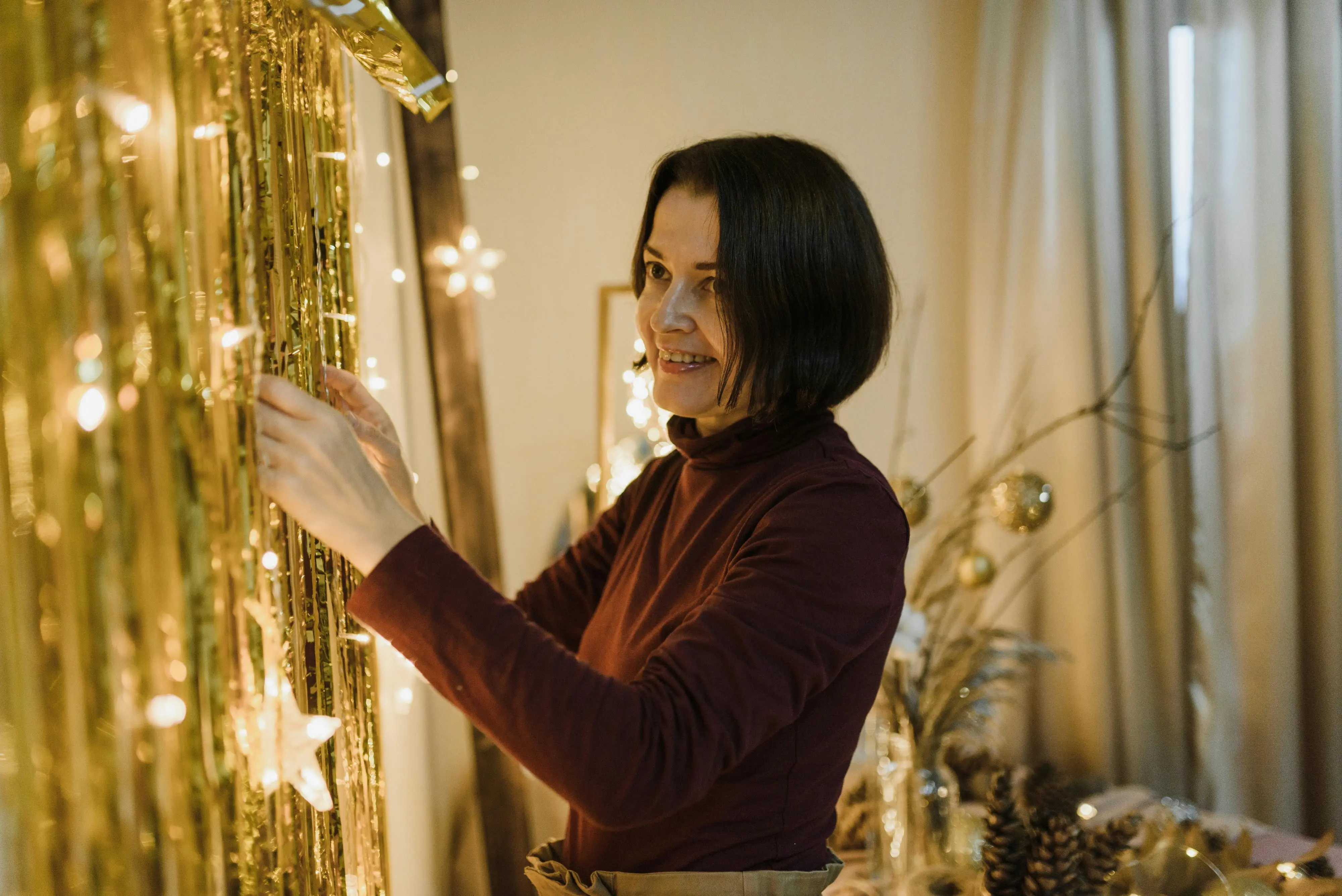 Smiling woman decorating her home with holiday lights, symbolizing preparing a Scarborough house to be clean, festive, and guest-ready for the season.