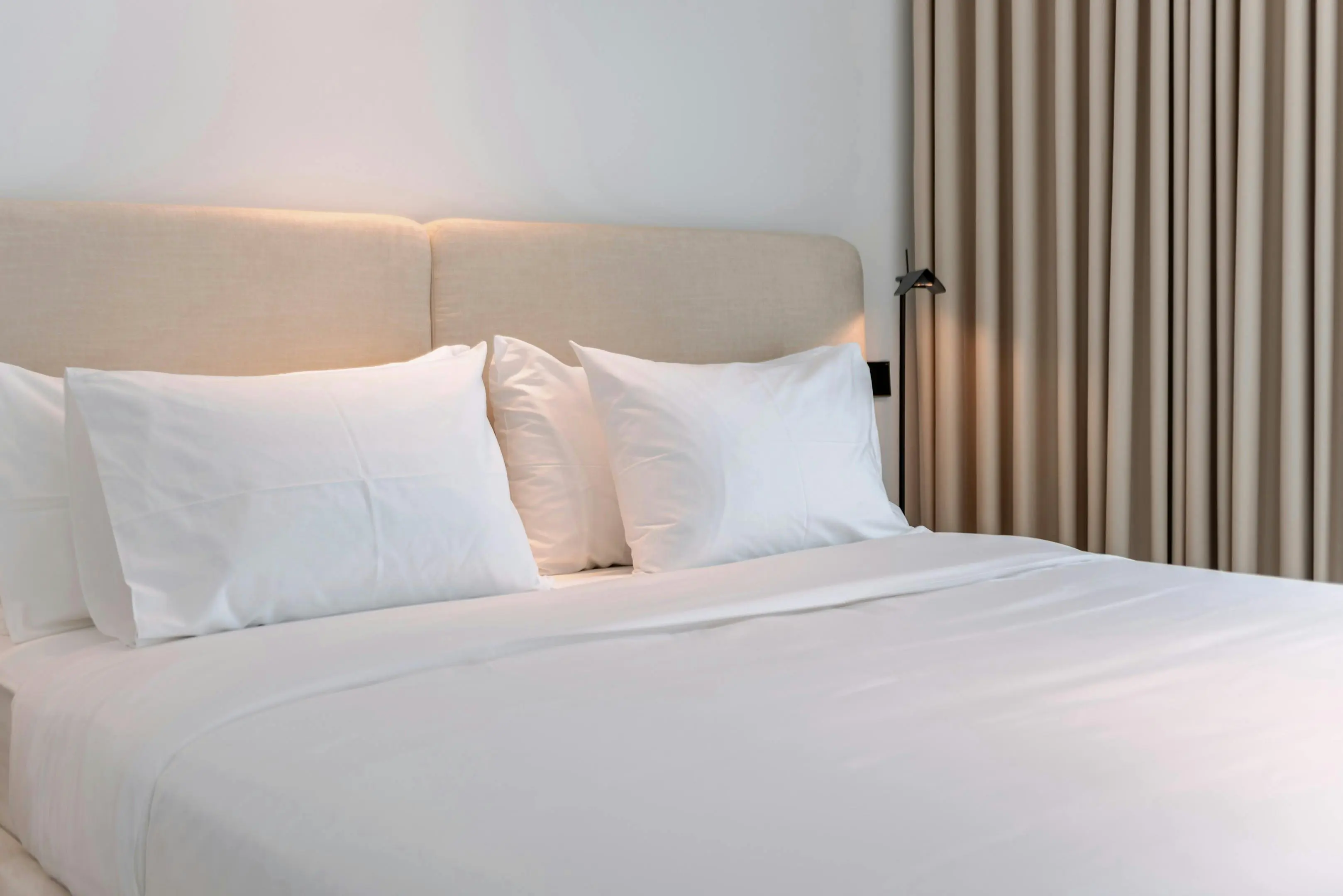 Freshly made bed with multiple white pillows neatly arranged, illustrating the importance of cleaning not just pillowcases but also the pillows themselves to remove dust mites, sweat, and allergens.