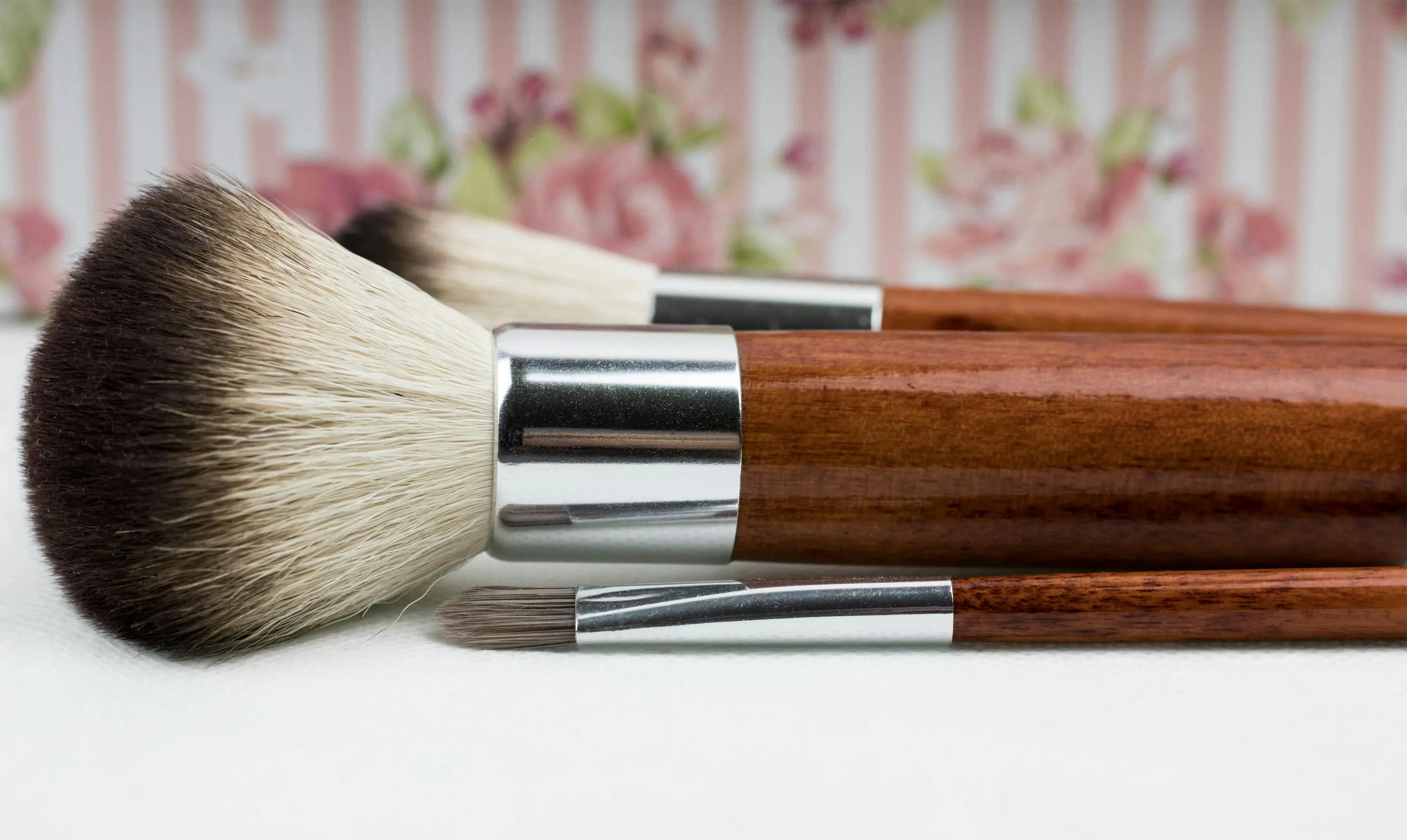 Close-up of wooden-handled makeup brushes with soft bristles placed on a white surface.