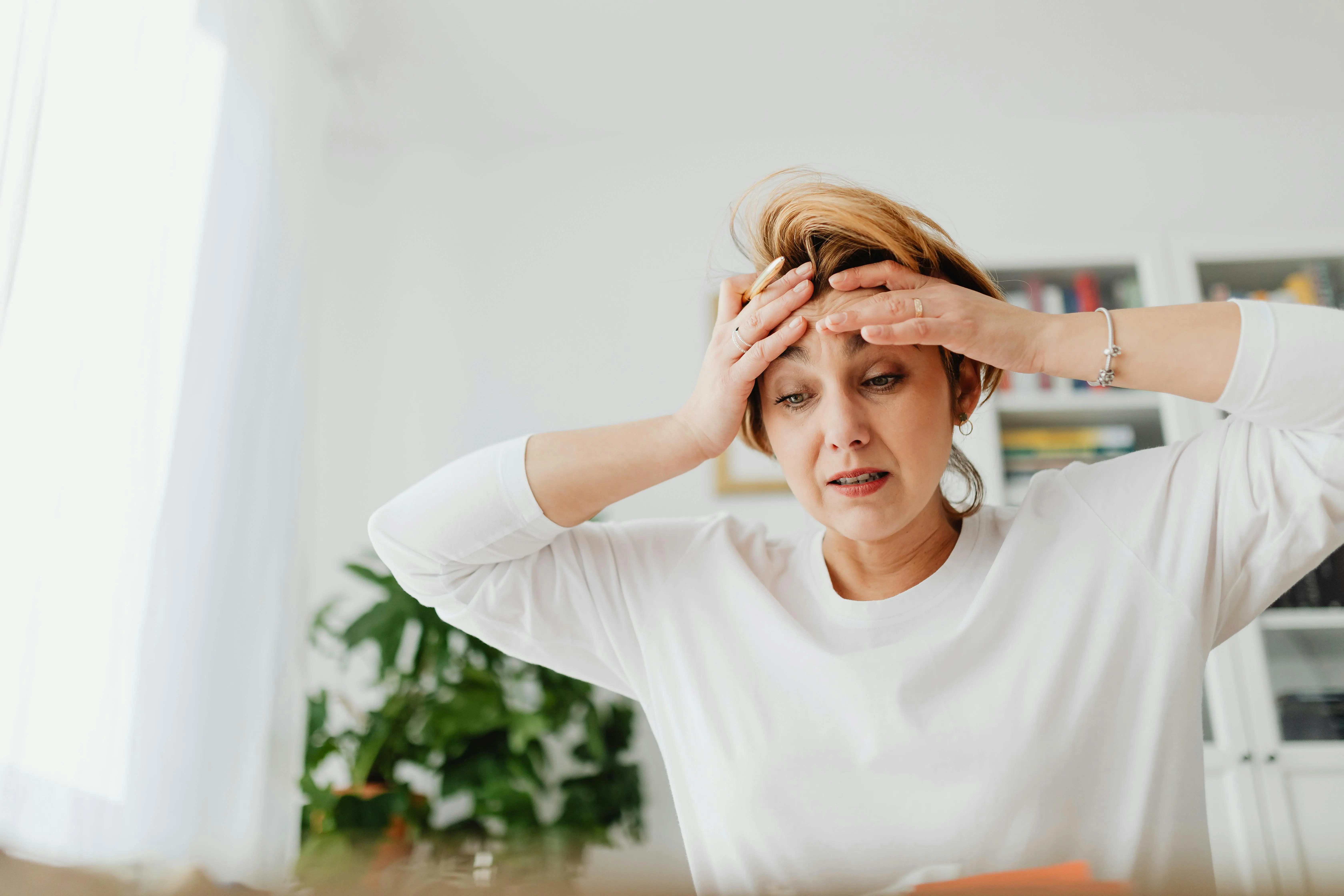 Frustrated woman holding her head in a bright home, highlighting stress and the need to upgrade from DIY to Etobicoke professional cleaning.
