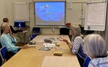 Grupp personer sitter runt ett konferensbord i ett mötesrum och tittar på en presentation med bergsbild projicerad på en duk