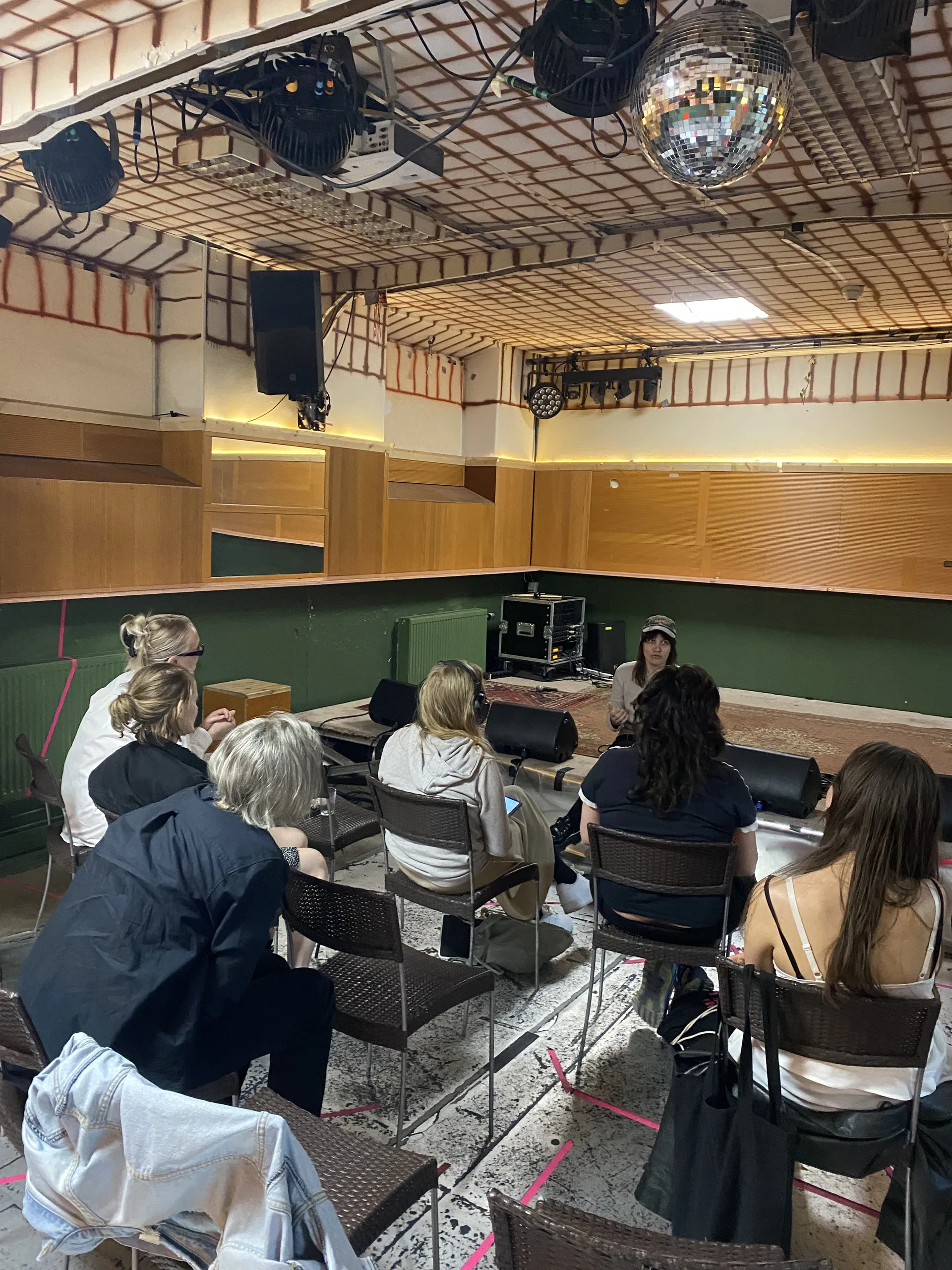 En grupp personer sitter på stolar och lyssnar på en kvinna som håller en presentation i en lokal med discokula i taket och scenbelysning