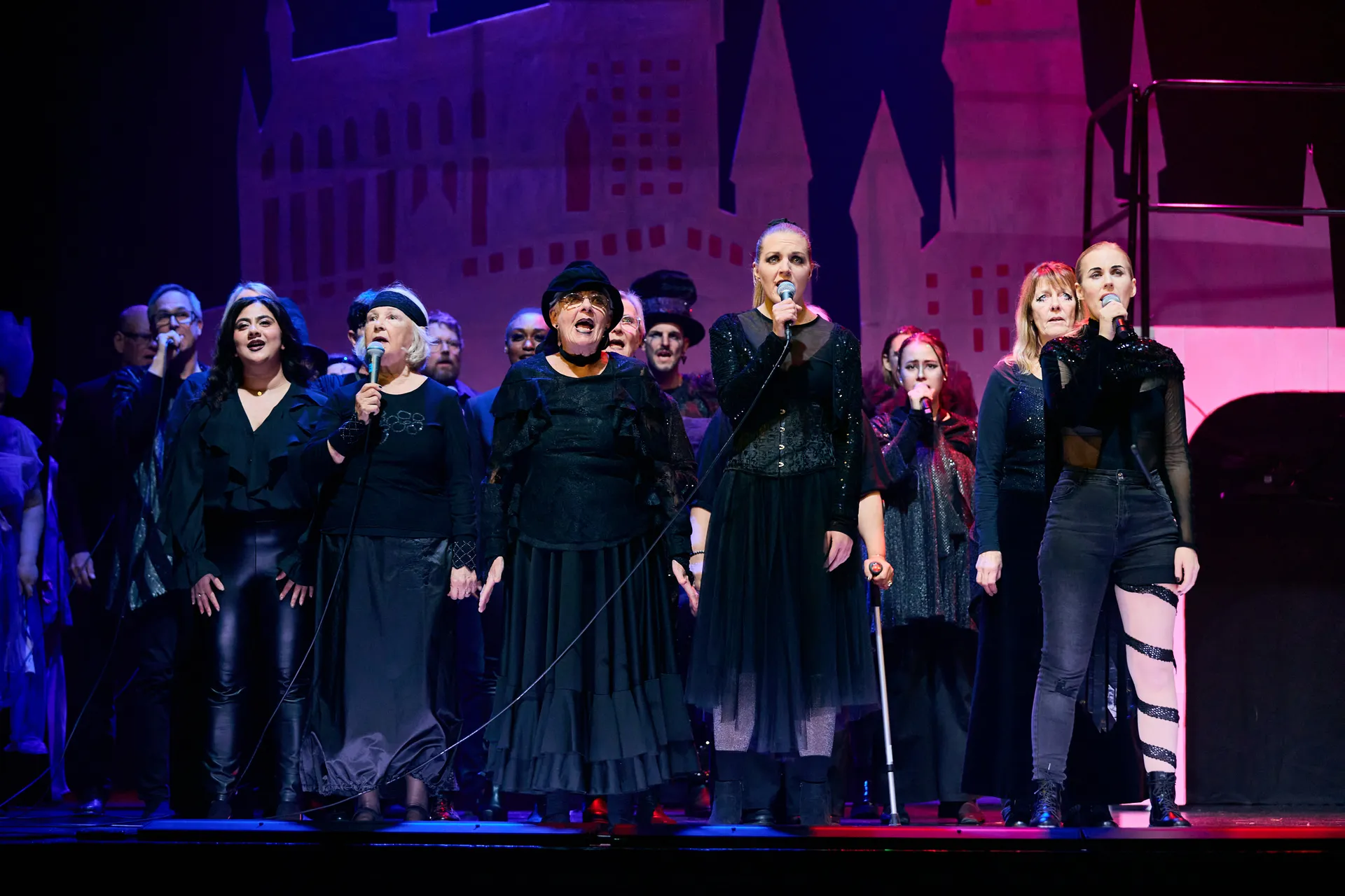 En grupp sångare klädda i svart uppträder på en scen med lila och rosa belysning och en slottssiluett i bakgrunden