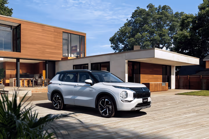 SUV branco estacionado em madeira ao lado de casa moderna com janelas grandes e parede de madeira.