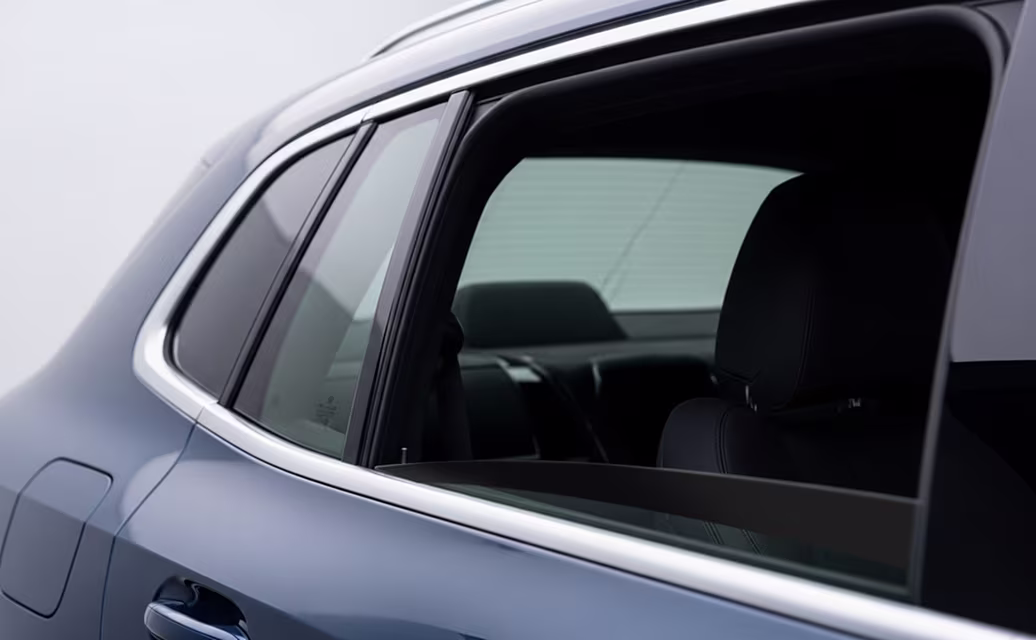 Detalhe da janela traseira de um carro cinza com assento preto visível pelo vidro.