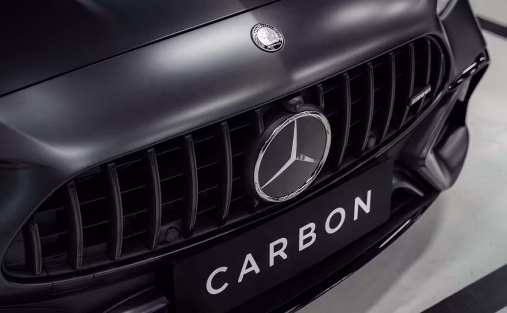 Close-up da frente de um carro preto com grade preta e emblema Mercedes-Benz no centro, placa com o texto 'CARBON'.