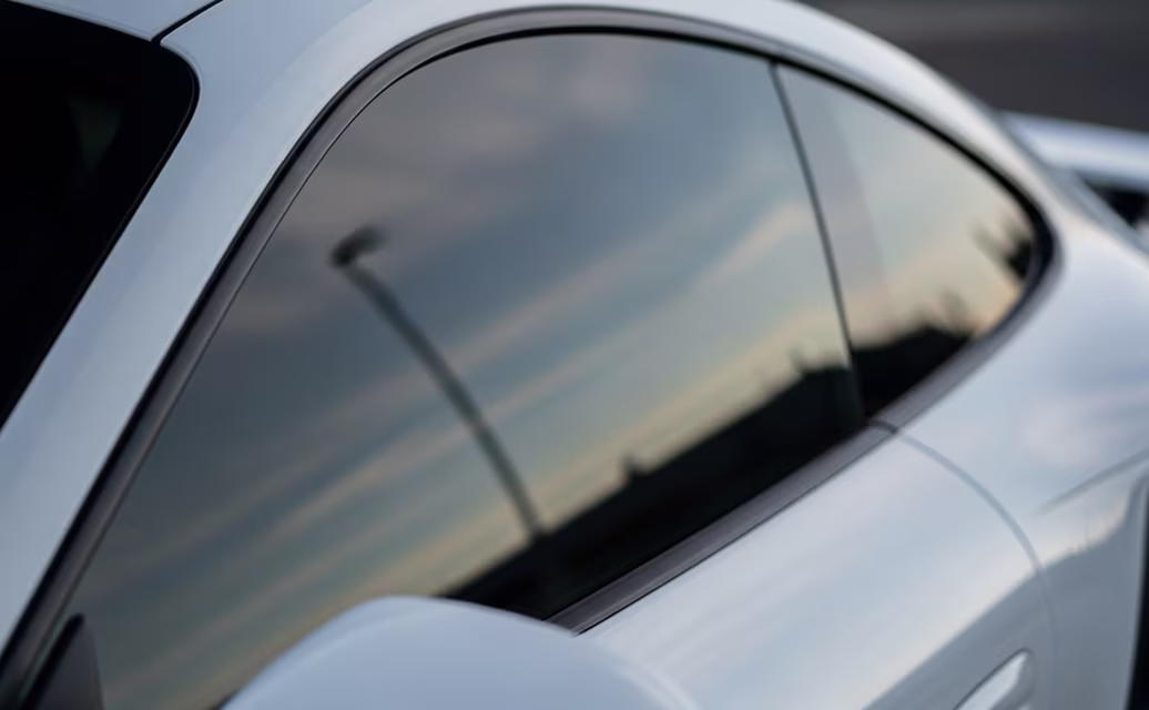 Reflexo da luz do pôr do sol na janela lateral de um carro prateado.