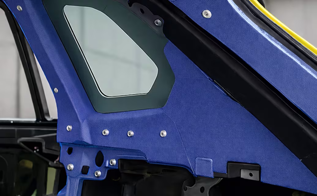Detalhe da estrutura interna azul de um carro esportivo com um pequeno vidro e fixações metálicas à vista.