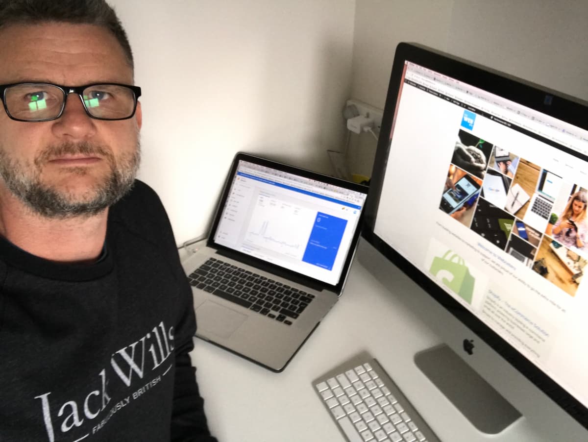 Portrait of Steve, founder of Webcetera, at his desk in 2016 with a laptop and iMac showing early website development work and analytics.