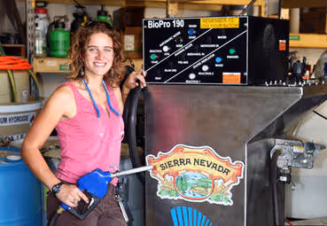 Smiling woman holding a blue fuel nozzle next to a Sierra Nevada branded fuel dispenser with BioPro 190 label.