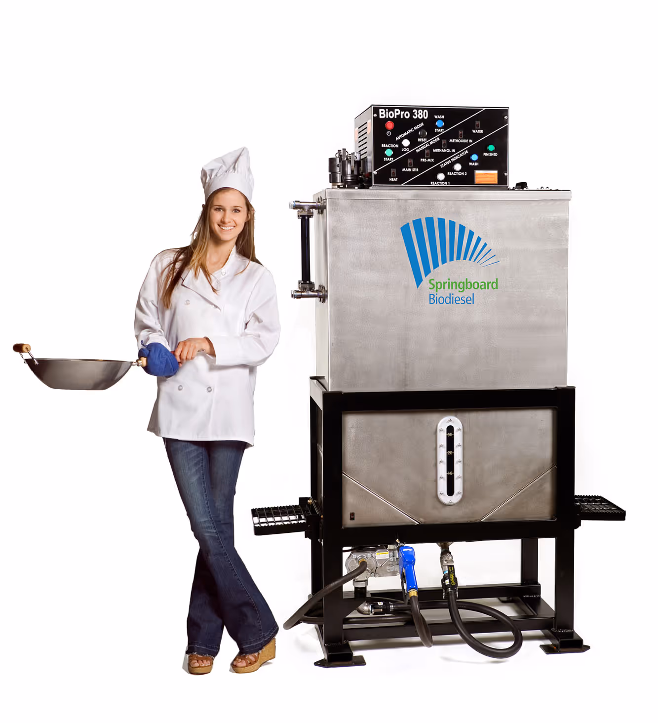 Woman in chef uniform holding a wok beside a large stainless steel Springboard Biodiesel machine.