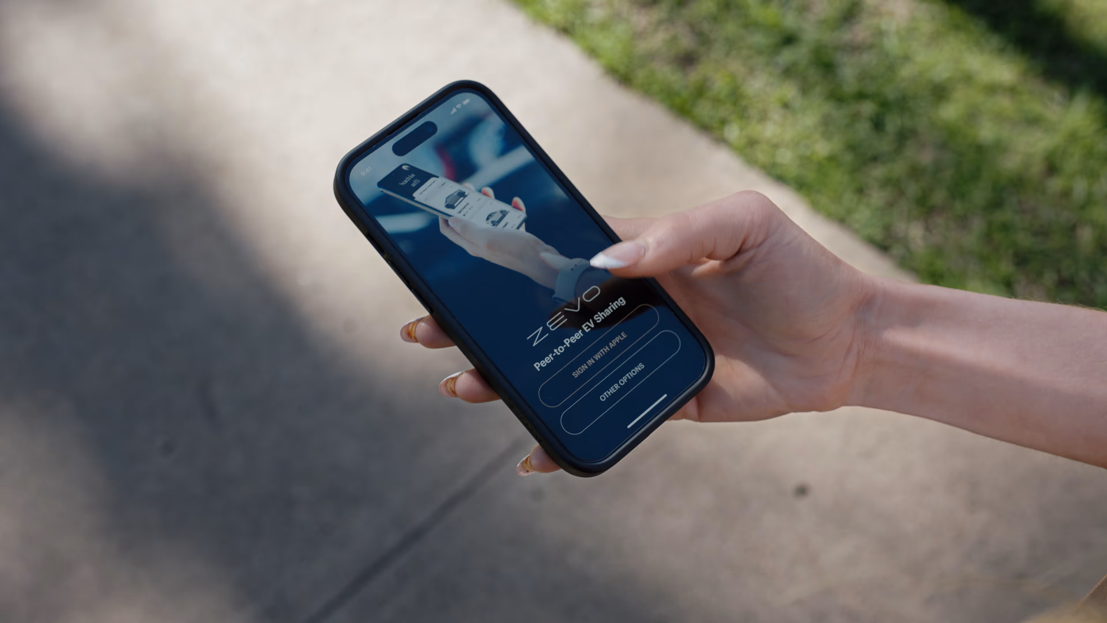 Hand holding smartphone displaying the Zevo app sign-in screen with options to sign in with Apple or other options.
