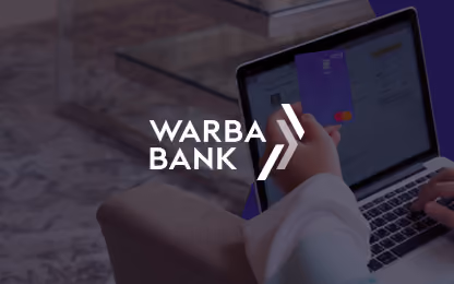 Person holding a card using a laptop with Warba Bank logo overlayed on the image.