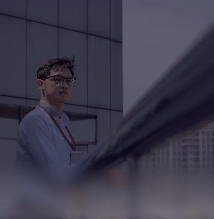 Man in glasses and white shirt standing by railing outside a modern building on a cloudy day.