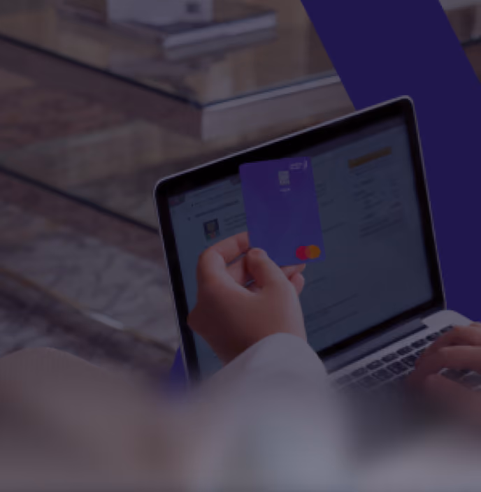 Person holding a purple credit card in front of a laptop screen showing an online banking interface.