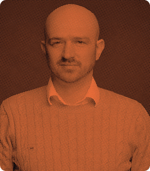 Portrait of a bald man with a mustache and goatee wearing a collared shirt against a textured background.