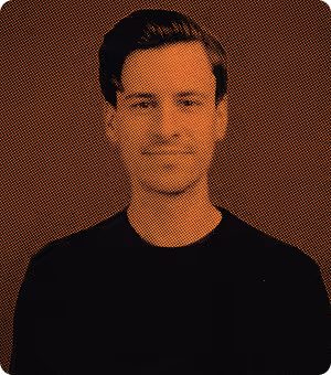 Portrait of a young man with dark hair styled back, wearing a black shirt against a dark background with a halftone orange overlay effect.