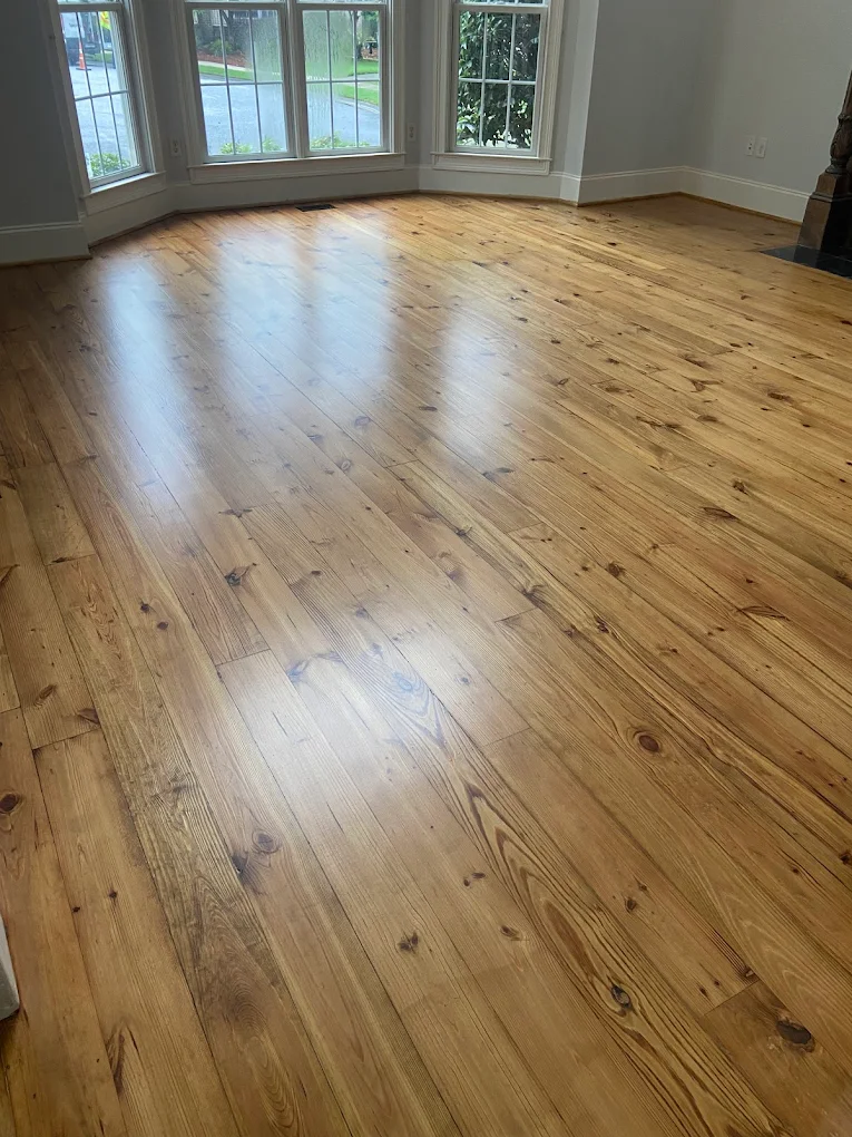 Empty room with polished light brown wooden floor and large windows letting in natural light.