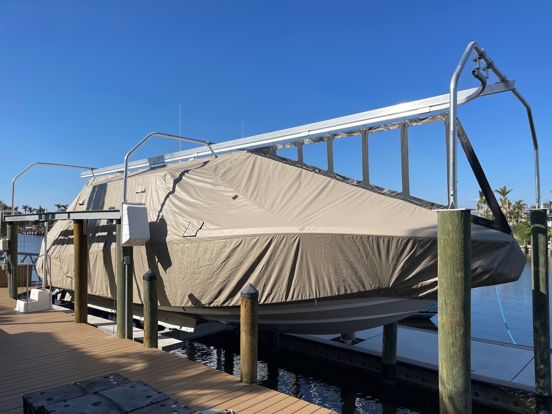 Tan Marine Concepts cover hanging from a bridge frame over an open boat lift