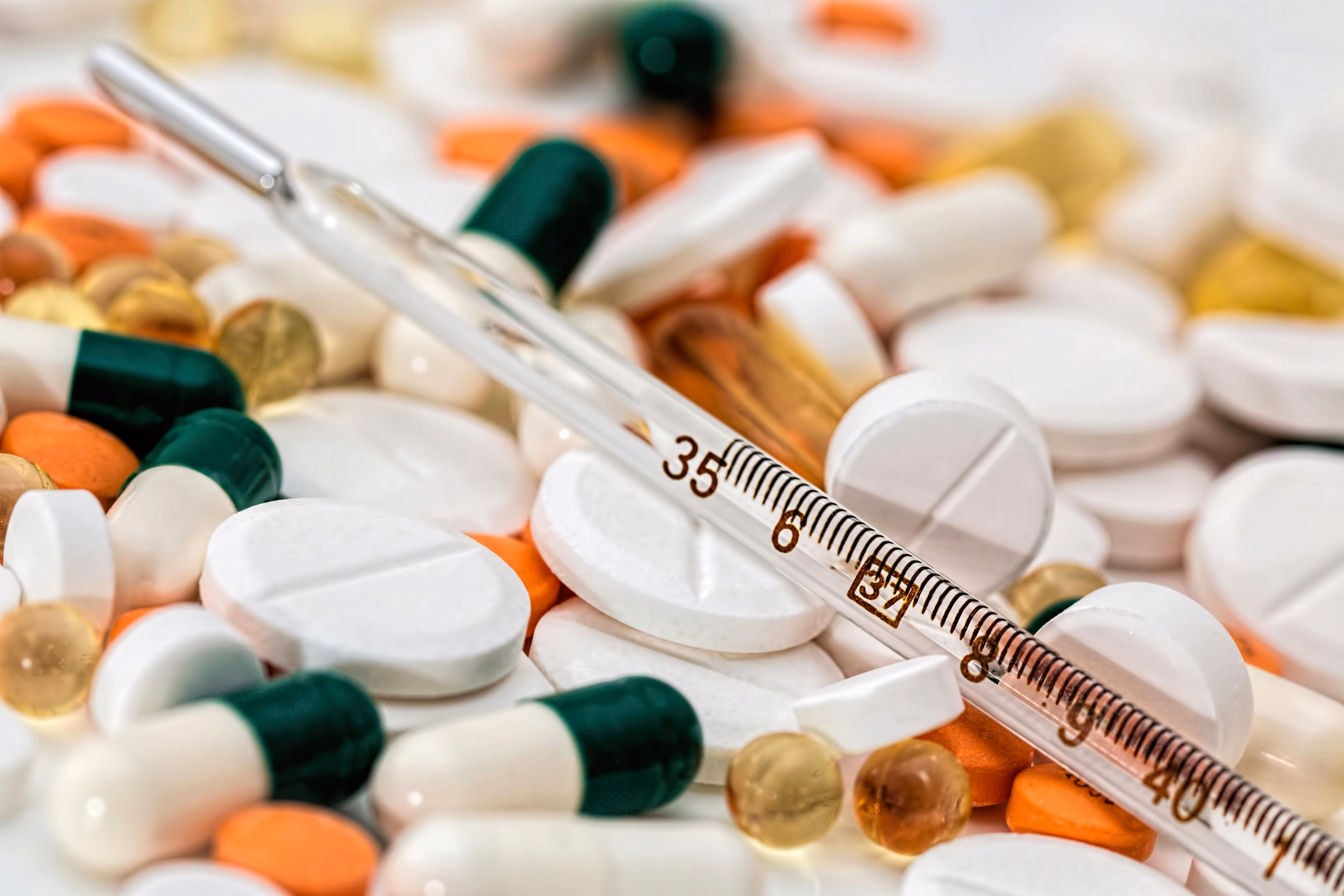 Close-up of assorted capsules and tablets with a glass thermometer on top.