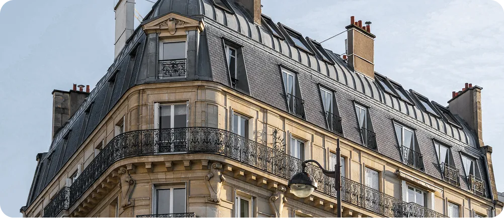 Top floors of a classic Parisian-style building with decorative wrought iron balconies and grey mansard roof under a clear sky.