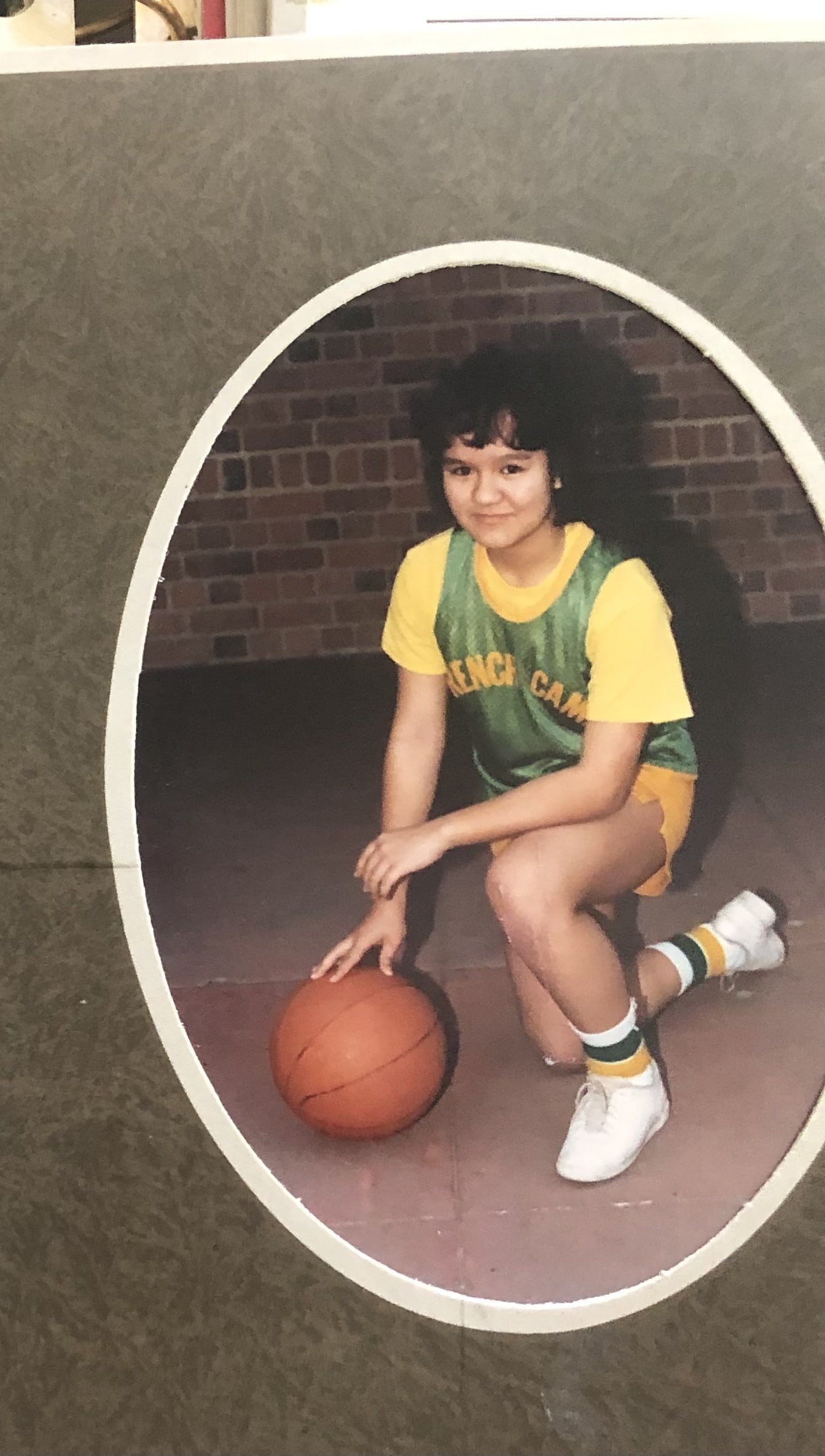 A young Precious kneeling in a basketball uniform while touching a basketball.a