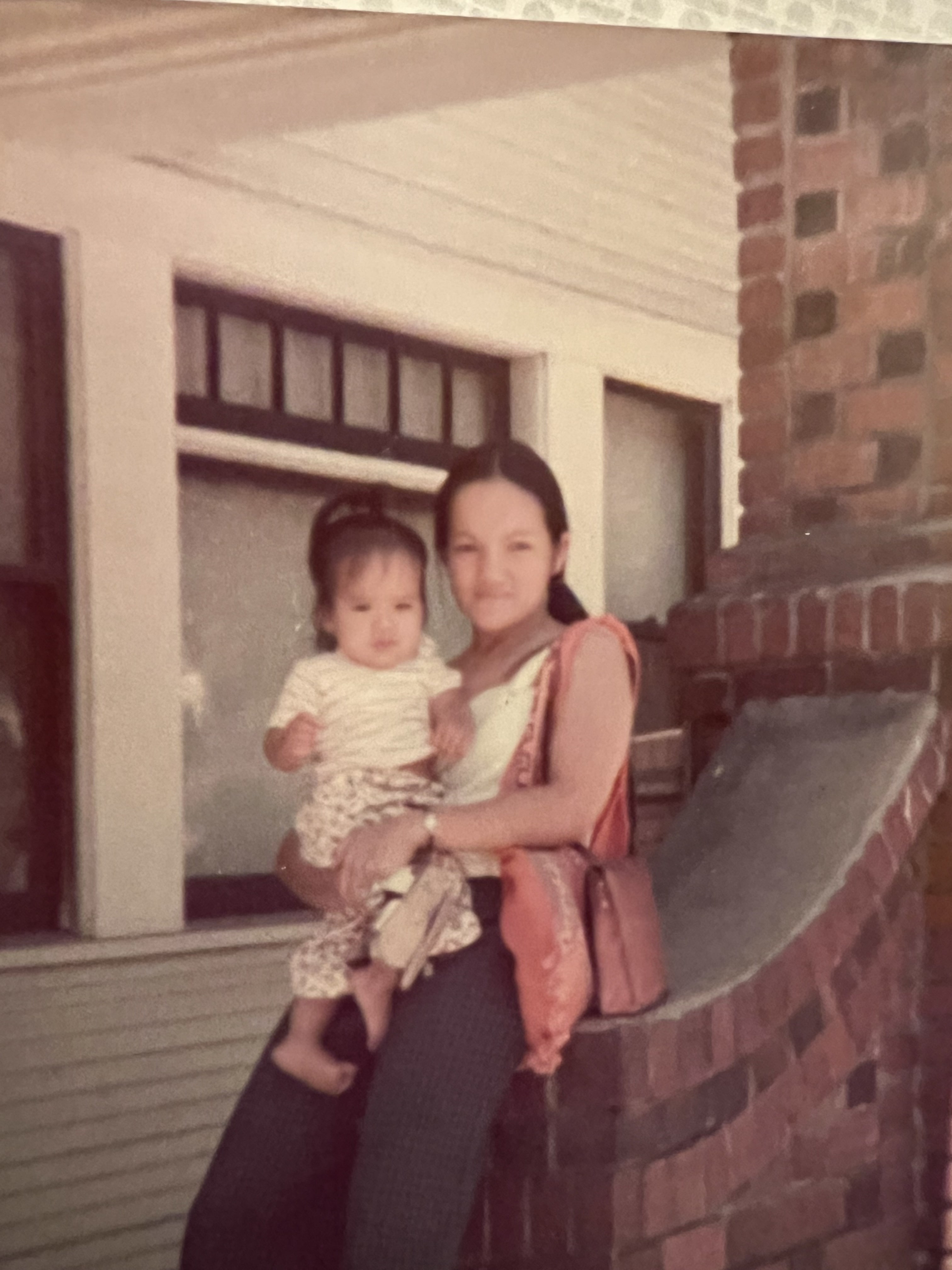 Precious' mother holds baby Precious while sitting on the edge of a brick porch.