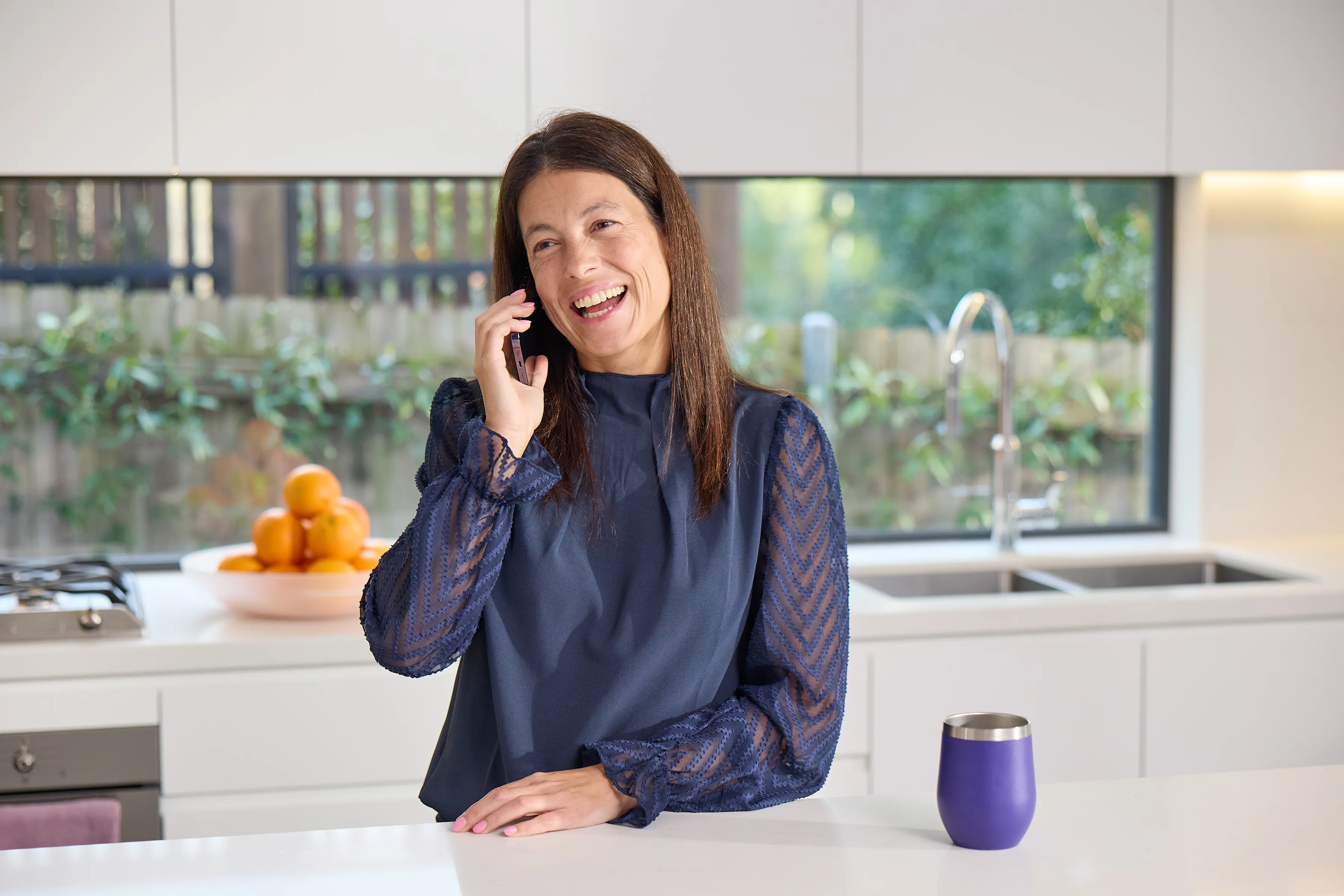 Smiling woman in her kitchen on a phone call about an ENT specialist referral