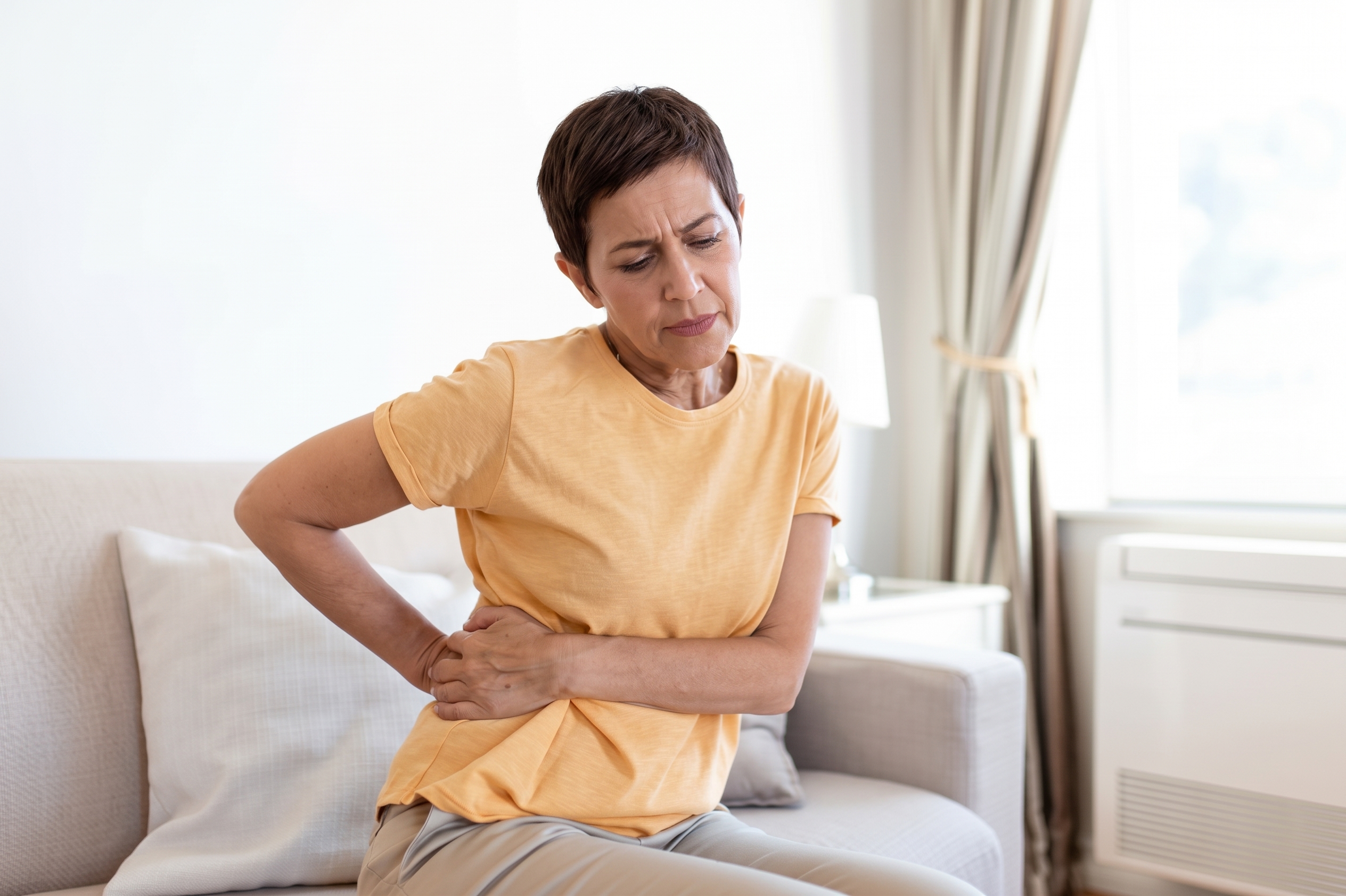 Woman on the couch holding her lower back in discomfort, worried about kidney infection symptoms