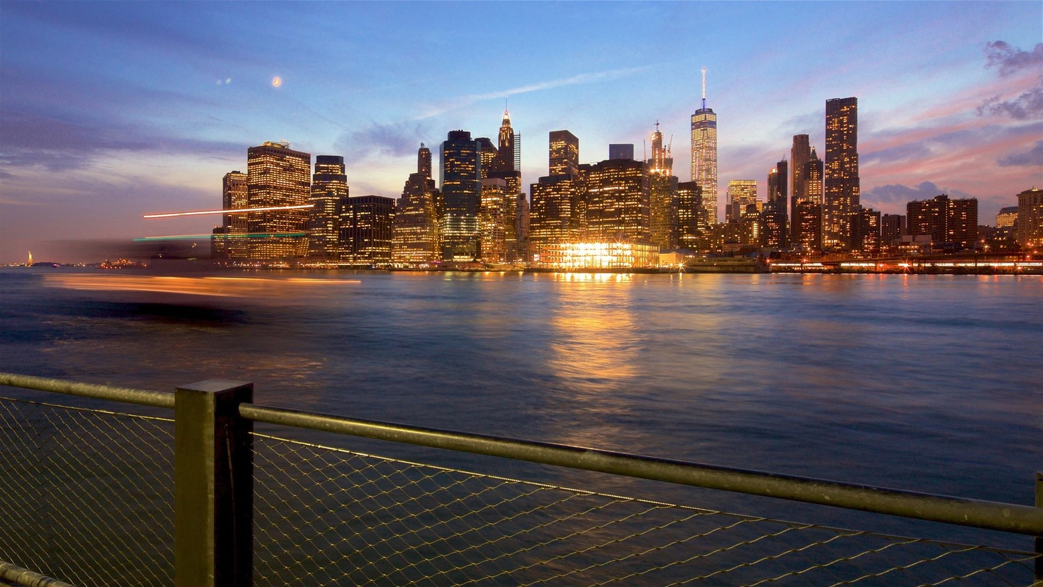 New York City skyline at sunset, viewed from waterfront with glowing buildings