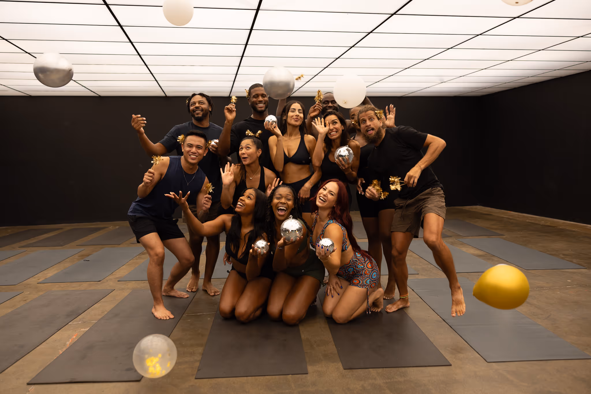 Diverse group of people posing playfully with disco balls in fitness studio