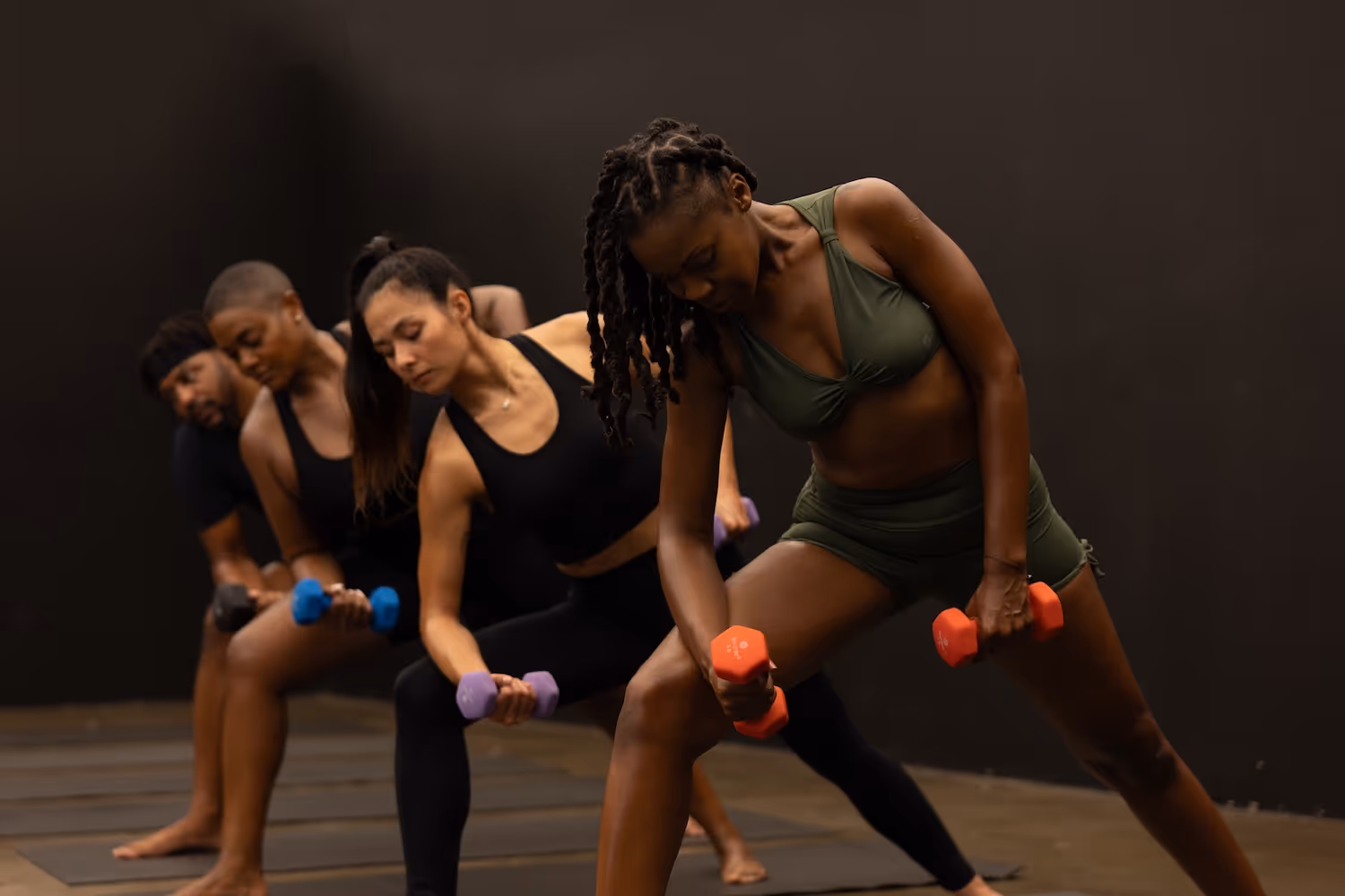 Group of people doing strength training with colorful dumbbells in dark studio