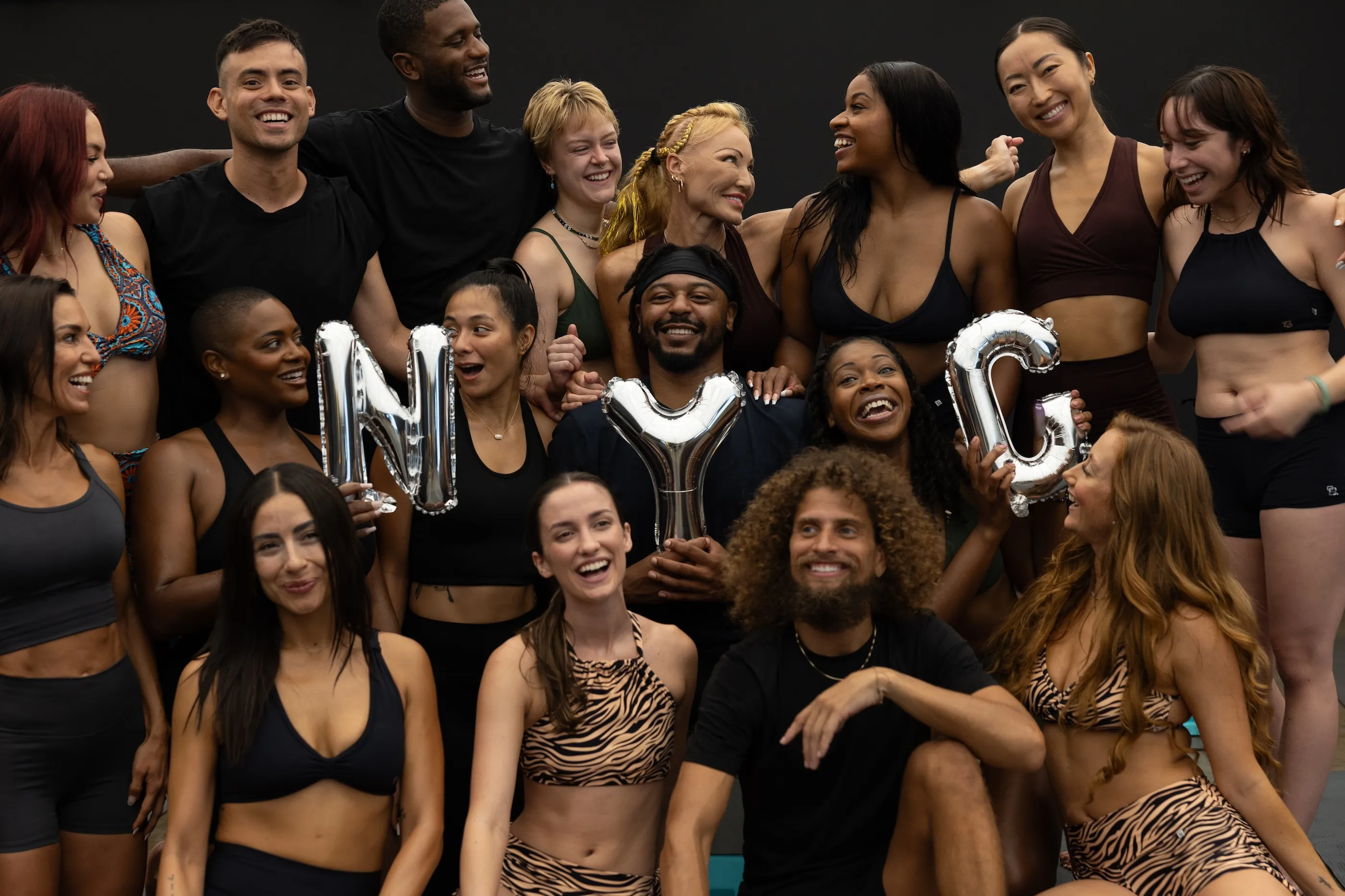 Diverse group of fitness enthusiasts holding NYC balloon letters, smiling