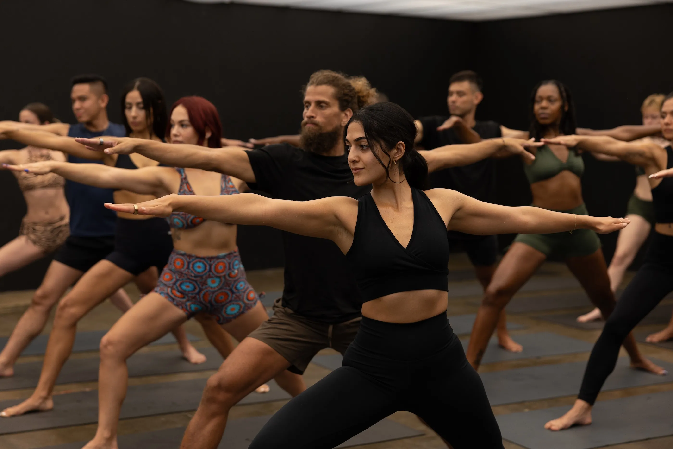 Diverse group practicing yoga warrior pose in a dark studio