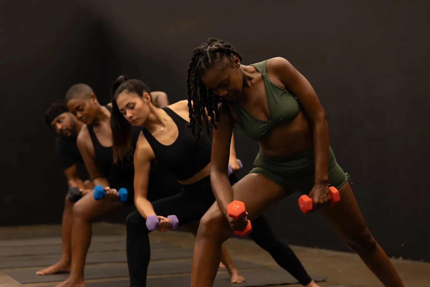 Group of people exercising with colorful dumbbells in fitness studio