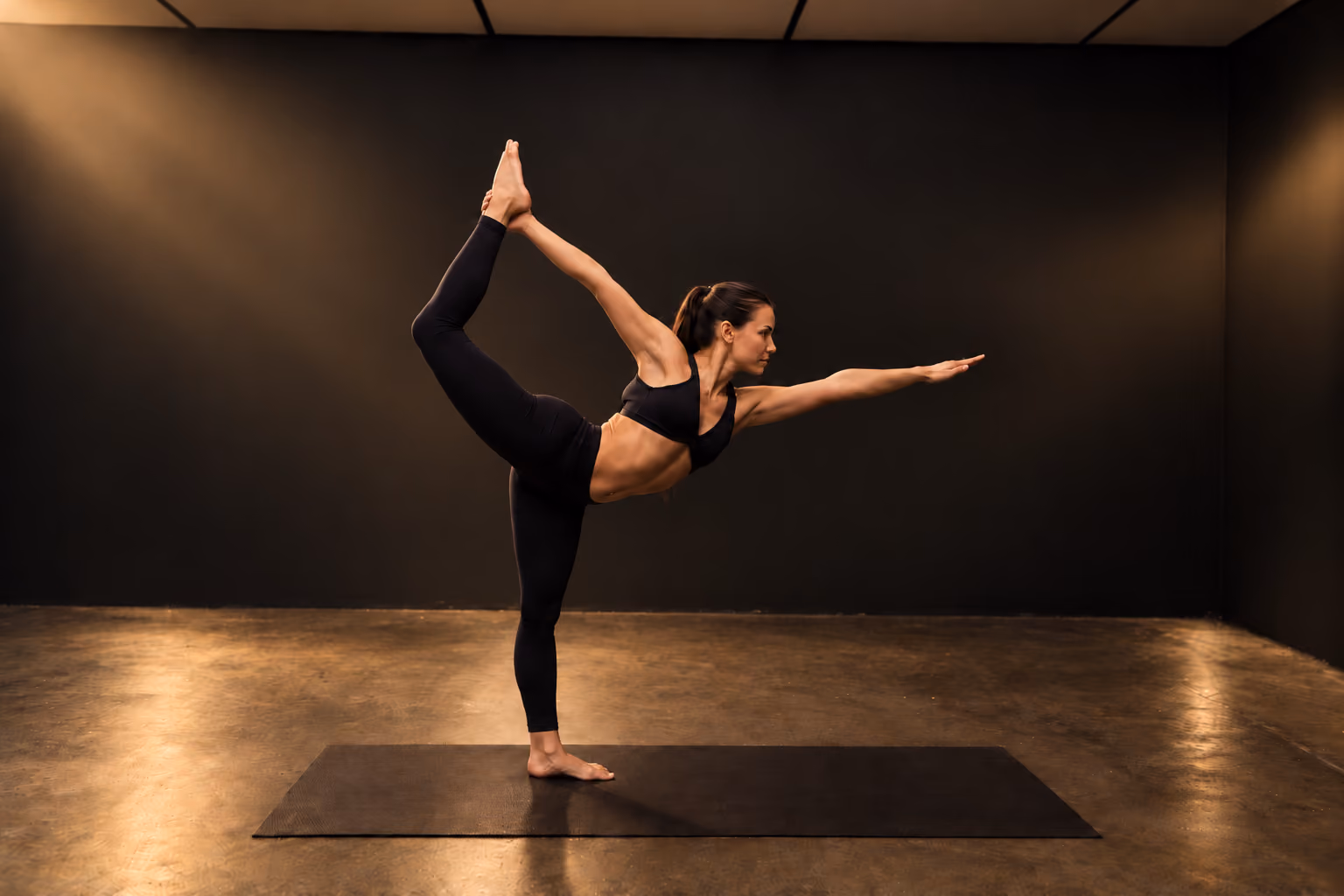 Woman performing yoga pose on mat in studio with dark walls