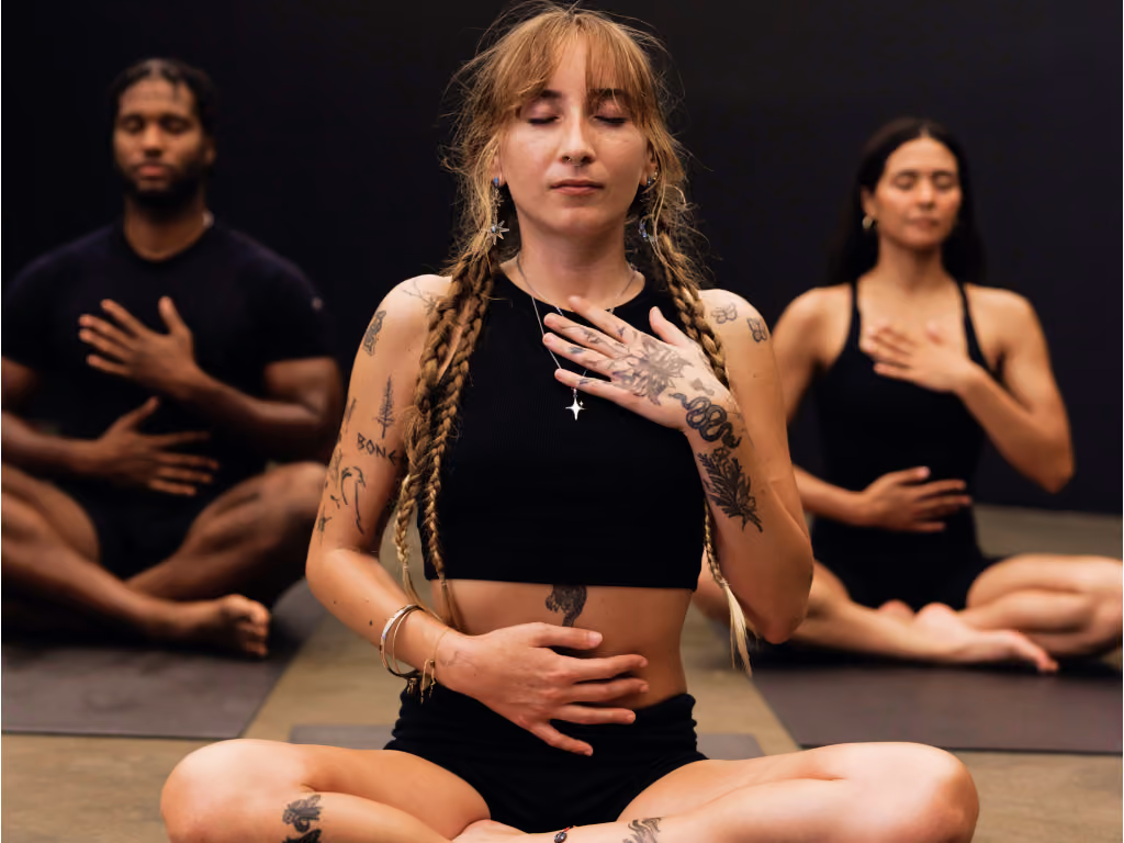 Woman with braided hair and tattoos meditating in cross-legged pose during group yoga session