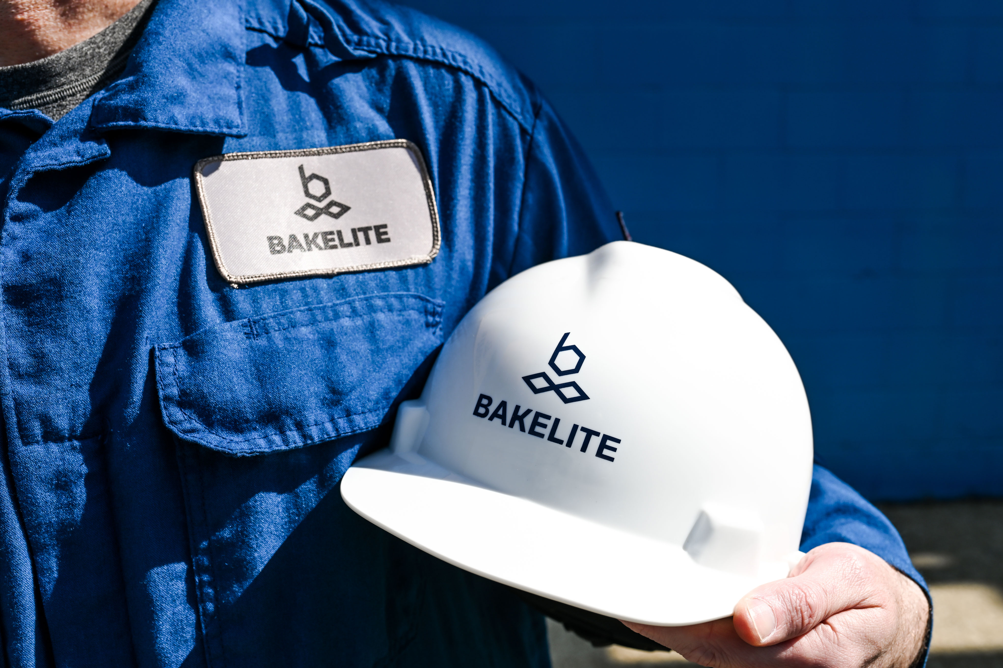 Person in blue work uniform holding a white hard hat with Bakelite company logo.
