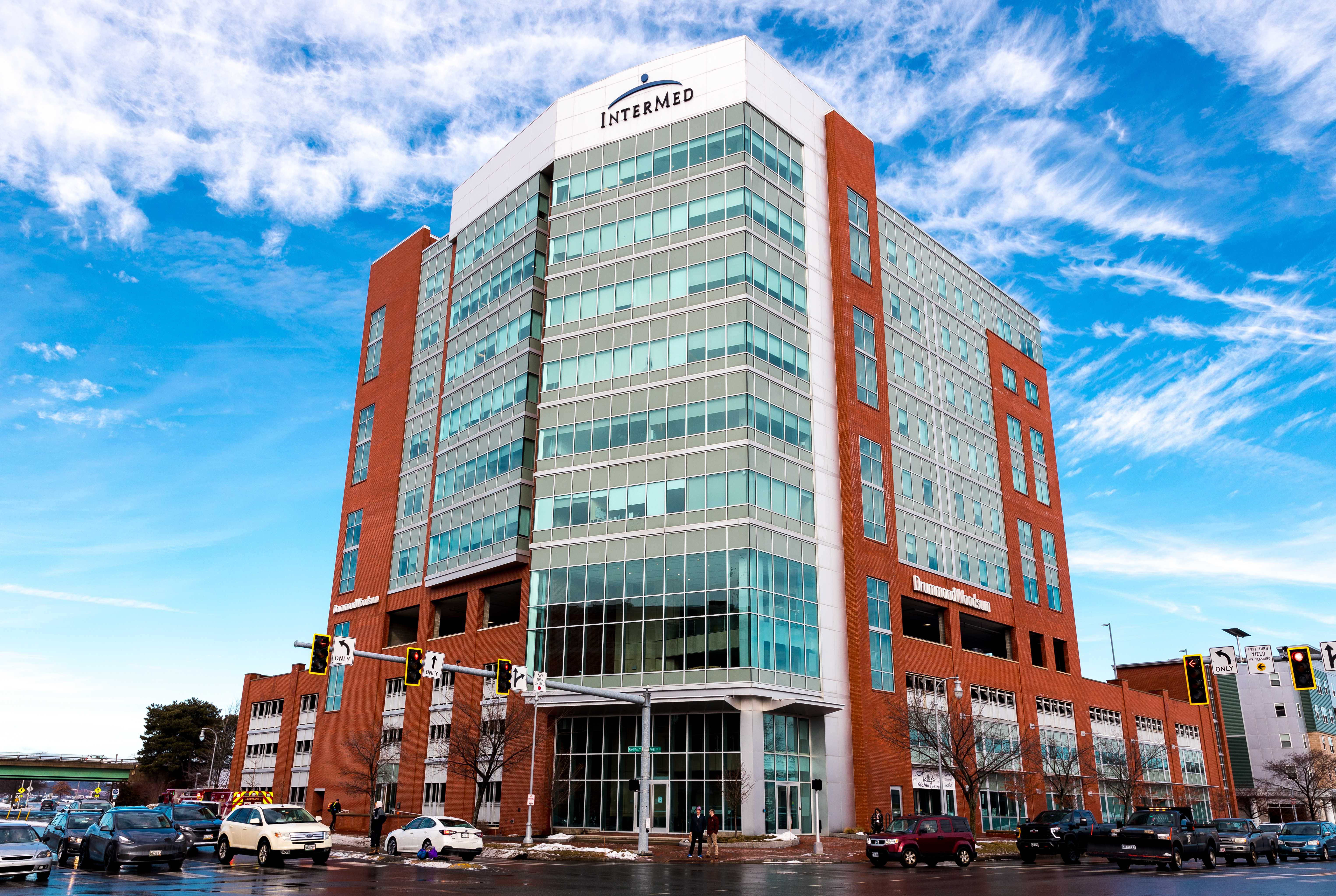 Tall InterMed building with glass windows and red brick facade under a blue sky with clouds.