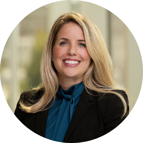 Smiling woman with long blonde hair wearing a black blazer and teal blouse.