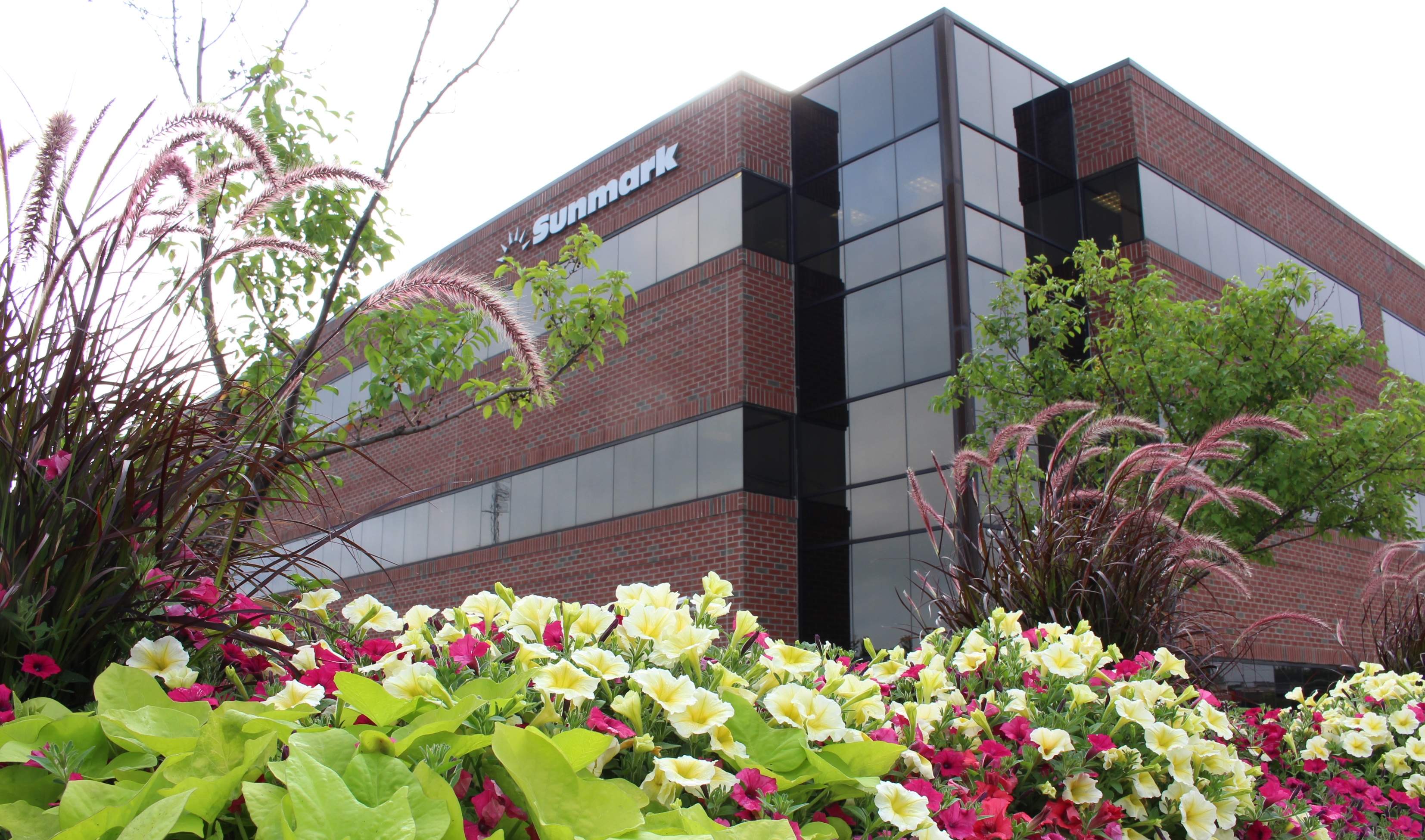 Brick office building with Sunmark logo, surrounded by bright yellow and red flowers and greenery.