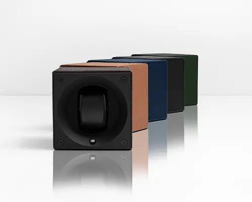 Four compact watch winders in brown, blue, black, and green leather lined in a row on a reflective surface.
