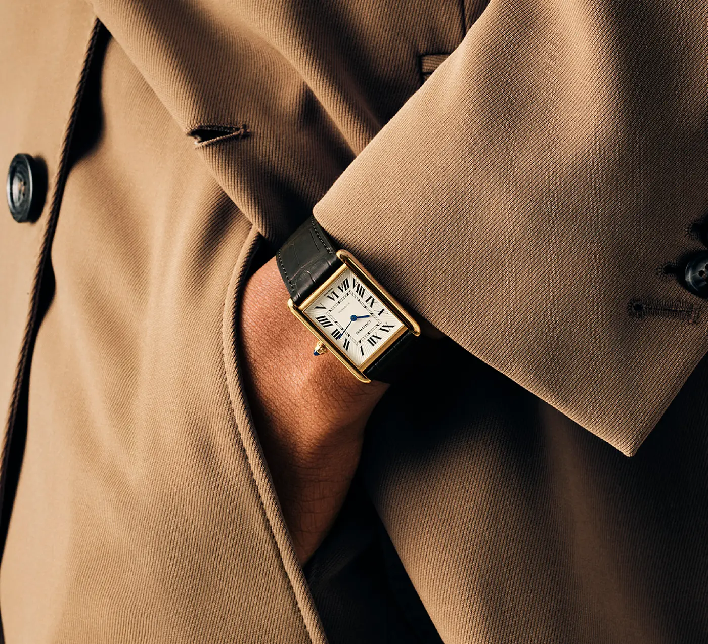 Close-up of wrist with a rectangular gold Cartier watch with black leather strap and Roman numerals.