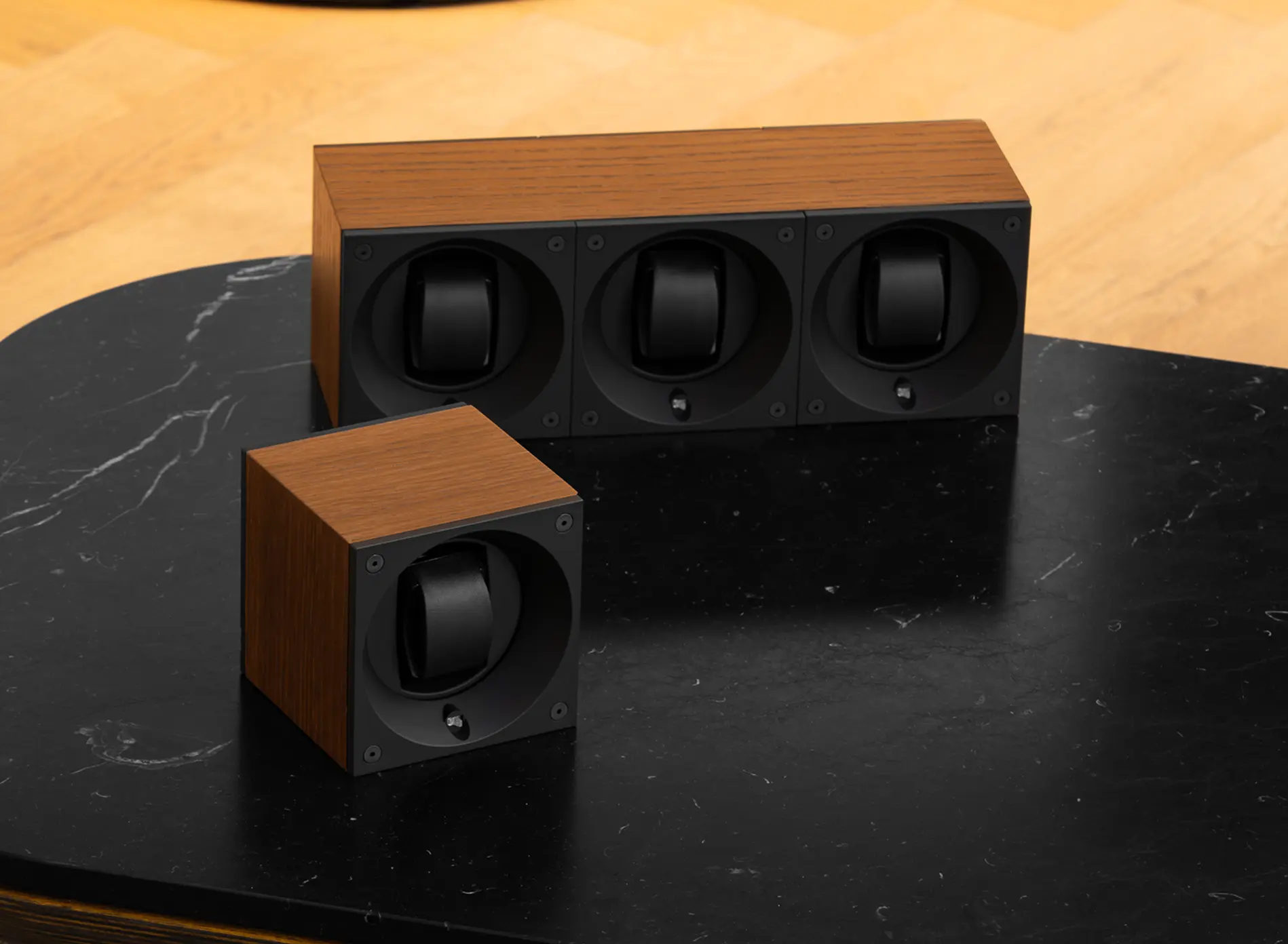 Wood-finished watch winders with black circular holders on a black marble table.