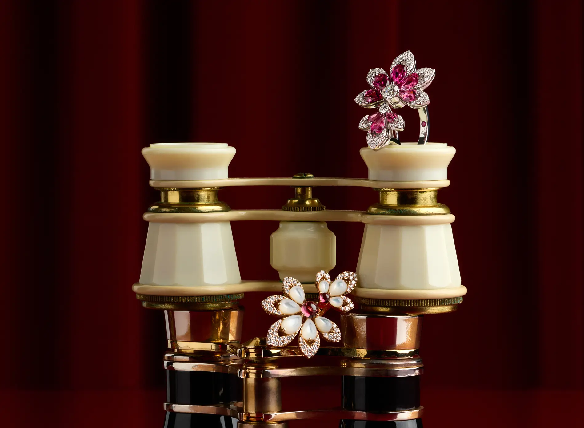 Vintage cream and gold opera glasses with two jeweled floral brooches, one on top and one in front.