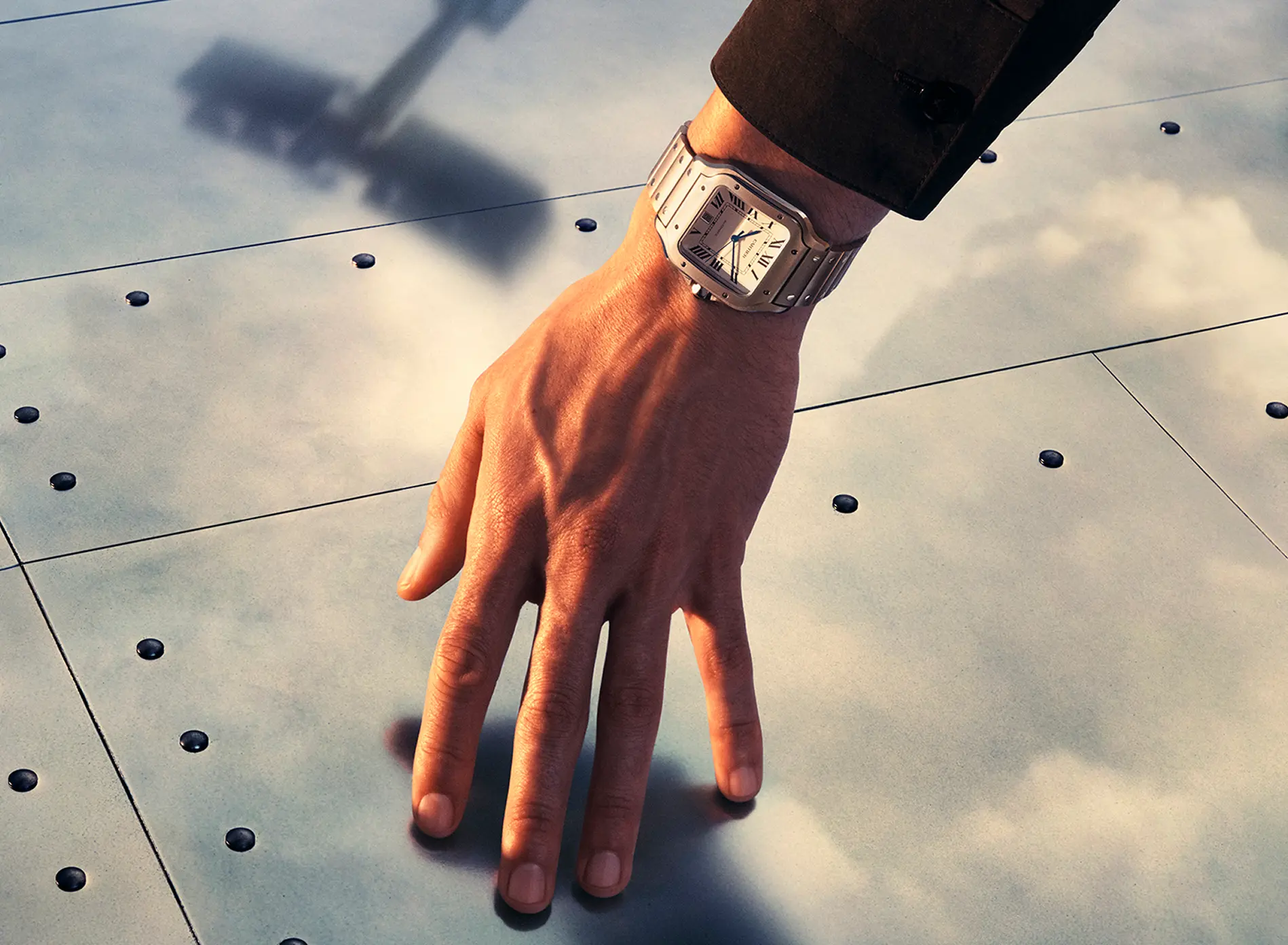 Close-up of a hand wearing a silver wristwatch with Roman numerals over a metallic surface.