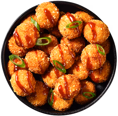 Een kom met knapperige, gefrituurde ronde snacks, overgoten met saus en gegarneerd met gesneden groene uitjes.