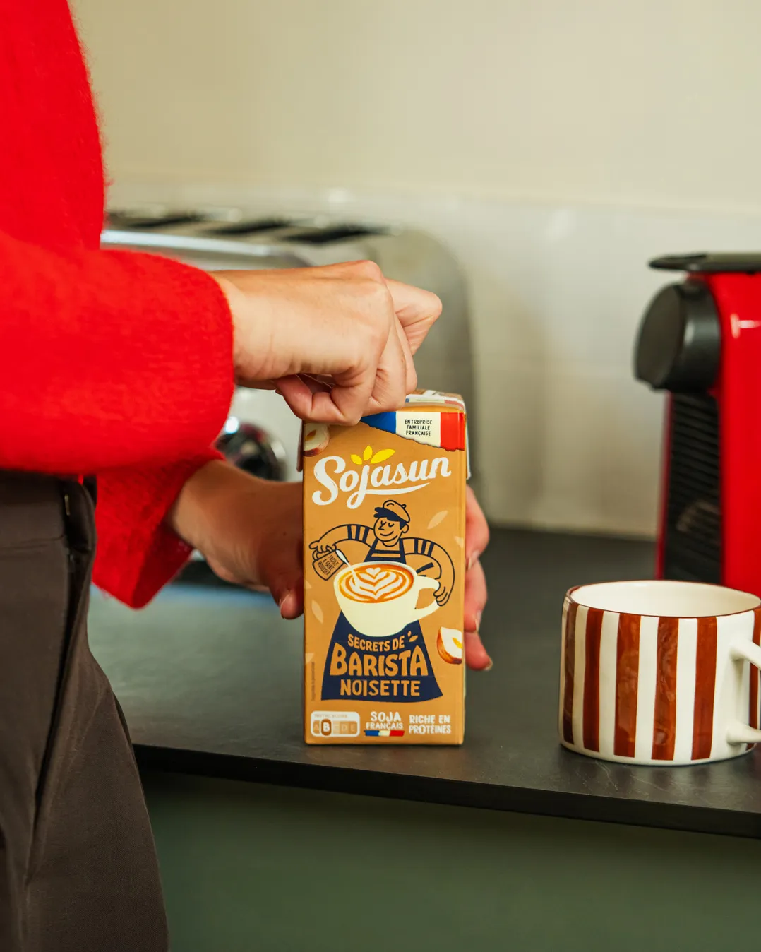 Boisson Sojasun barista noisette à côté d'une tasse rouge sur un plan de travail de cuisine