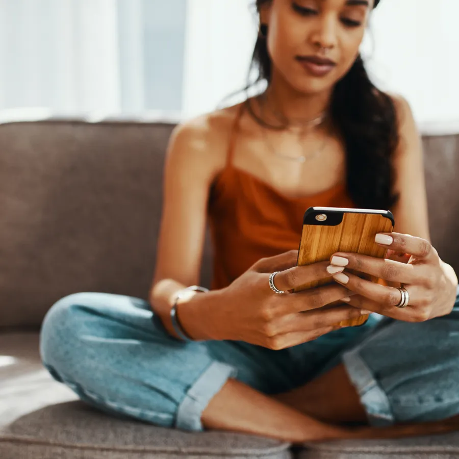 Une femme fait défiler des profils sur son téléphone, assise dans son canapé
